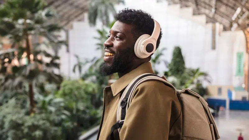 Homem usando fone de ouvido Bluetooth com cancelamento de ruído, curtindo música enquanto caminha em ambiente urbano